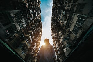 A photo taken from the ground of a woman standing between two very tall buildings.