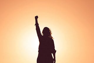 Woman as shadow figure raising the fist in the air and an orange sunny background