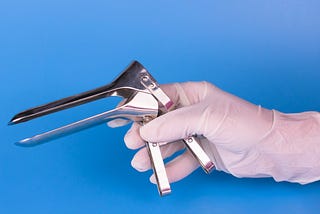 Gynecological mirror in the hand of a doctor on a blue background.