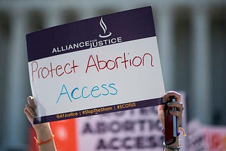 A woman holding up a sign that says “Protest Abortion Access.”