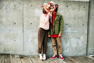 Couple kissing behind bouquet of flowers.