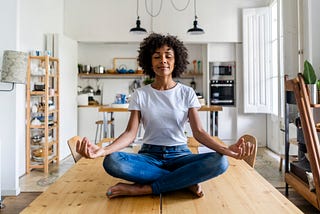 A photo of a black woman meditating while sitting on top of her table.