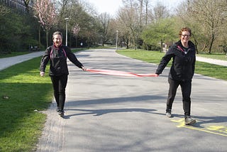 Two women holding a pink scarf practice social distancing and keep 1.5 meters at the park on March 27, 2020 in Amsterdam.