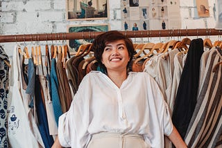 Woman smiling in front of a rack of clothes.