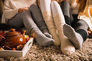 Three young women sit close together, a tea kettle nestled in the front with seasonal items.