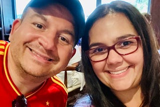 A smiling selfie of a man and woman. He is wearing a soccer shirt of the Spanish national team.