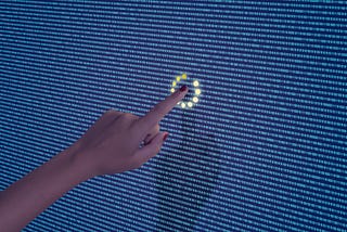 A photo of a finger touching a line of code on a screen. There is a loading ring around the word that has been touched.