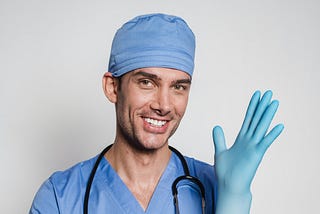 Male doctor grinning while putting on exam glove