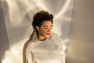 A woman leans against a wall with her eyes closed.