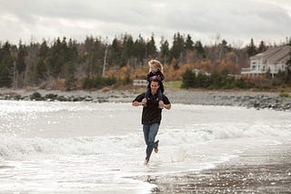 Author with his daughter on his shoulders running in the surf on the beach
