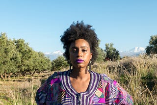 A confident Black woman standing against a prairie-like background.