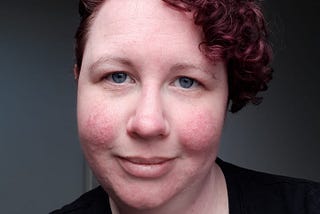 Kelley, the author, is pictured with a short curly pixie hairstyle. Her hair is curly and dyed a purple-maroon colour.