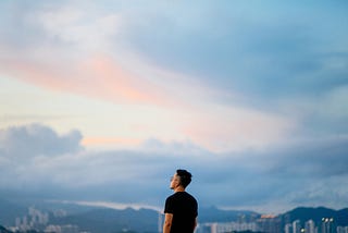 A man looks out at the sky and cityscape.