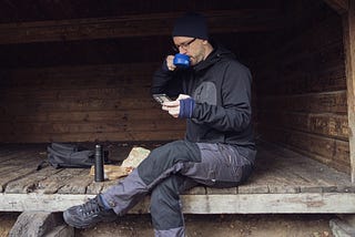 Me sitting in a hiking shelter having a coffee and looking at my phone