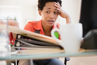 A photo of a frustrated black woman sitting at her desk at work.