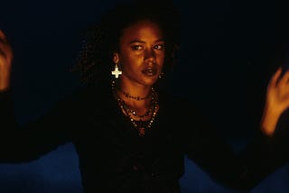 Screenshot of Rachel True from “The Craft.” She is wearing black and many necklaces.