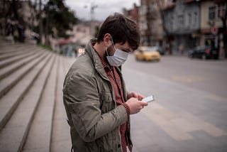 A man wearing a face mask types into his phone.