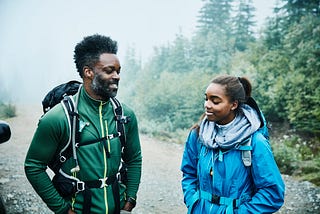 A smiling father and daughter stand and talk next to each other while preparing for early morning hike.