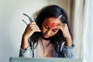 Shot of a young woman suffering from a headache while using a laptop at home.