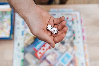 A hand holding two dice above a monopoly board game