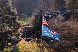 An American flag and a Trump flag flying over a burned down house.
