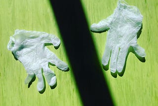 2 used surgical gloves on a green surface with a rectangular shadow falling between them.