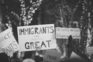 A black and white photo of people holding up hand made signs in support of immigrants and immigration.