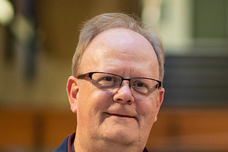 headshot of Dr. Thomas Hillen. Wearing a blue jacket, burgundy shirt and glasses.