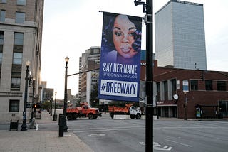 A street banner with an image of Breonna that says “SAY HER NAME BREONNA TAYLOR #BREEWAYY.”