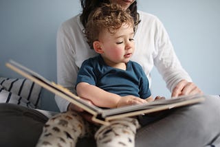 A photo of a mom reading a book to her child sitting in her lap.