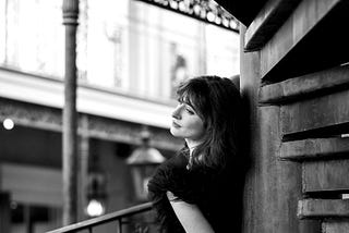 A black and white potrait of a woman standing on a balcony.