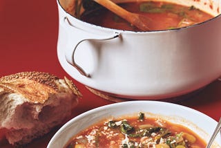 A pot of soup, a bowl of soup, and a small, rustic loaf of bread.