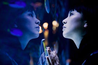 A woman at an aquarium looking at fishes in a tank. Cast in bluish light.