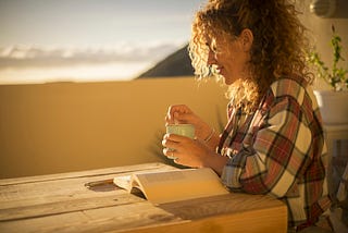 Woman holding mug, reading a book outside