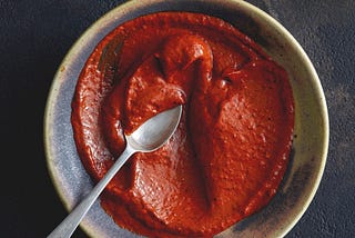 Overhead shot of a brown ceramic bowl with chile paste and a spoon in it.