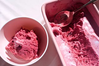 A fresh scoop of deep purple berry ice cream from a carton of the same rich looking ice cream.