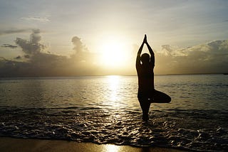 Figure in yoga position on shallow water on beach