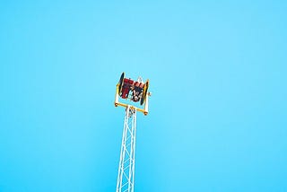 A person on a two-seater carnival ride that flings people upside down, which it is currently doing in front of a cloudless blue sky.