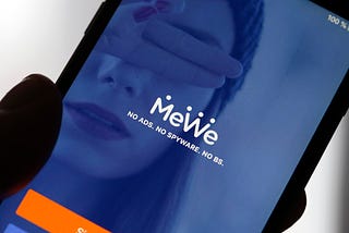 A photo illustration of the home page of the social media application MeWe displayed on the screen of an iPhone.