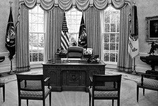 The presidential desk with empty chairs facing it in the Oval Office. Black-and-white photo.