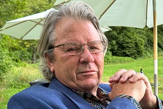 Headshot of George Phillips, outdoor umbrellas and a grassy expanse in the background
