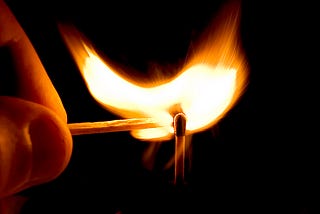 Closeup of a hand using a lit match to light another match.