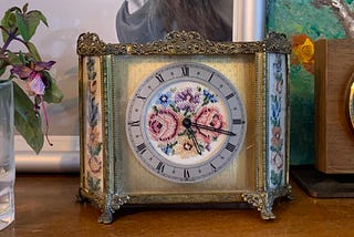 an old gilt clock, with a silk face embroidered with flowers, sat on a bookshelf.