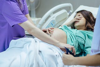 A doctor examines the belly of an expectant mother in the hospital room.