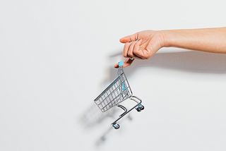 A mini shopping cart dangles off a person’s finger.