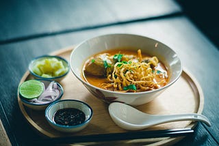 A bowl of ramen soup with dipping bowls of soy sauce, sliced onions, and other condiments.