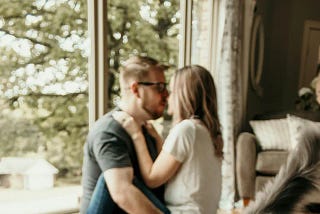 In the background a woman sits in the lap of a man, kissing him. In the foreground is a cat.