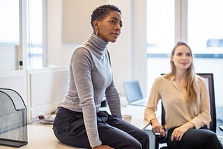 A photo of a black woman in a work meeting with a perplexed expression.