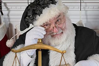 A picture of Emoluments Claus, a Santa Claus figure wearing all black robes holding the scales of justice.