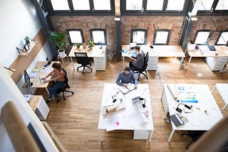 Office workers at their desks in a modern office. Half of the desks are filled, while the other half are empty.